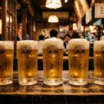 Five draft beers lined up on an izakaya table, just poured, still cold. The glasses are identical. Nobody has touched them yet. Warm amber light.
