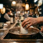 Sake Temperature: Why Warm Is Not a Compromise A small white ceramic tokkuri (sake flask) sitting in a bowl of hot water on an izakaya counter, gently warming. Steam rises. A small ceramic cup beside it. Winter evening light.