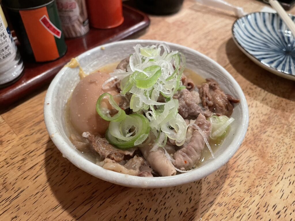 Nikomi: The Stew That's Been Simmering Since Before You Arrived 2 Japanese motsuni stew in a small bowl at an izakaya counter, topped with sliced green onions and served with daikon radish and pork offal in a light broth.