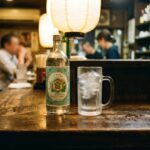 Kinmiya: The Shochu That Became the Working-Class Standard A bottle of Kinmiya Shochu on an izakaya counter — the distinctive green label, the clear spirit inside. A frozen mug beside it. The counter is worn. The light is warm.