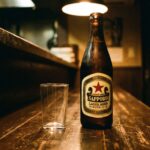 Akaboshi: The Beer That Tells You What Kind of Place You're In A classic Sapporo Lager bottle — the red star label — on a worn izakaya counter. Dark wood, warm light, nothing decorative. The bottle is cold. The glass beside it is plain.