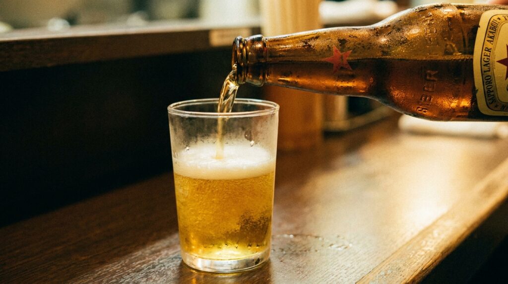 A close-up of an akaboshi bottle being poured into a plain glass tumbler. The beer is golden. The pour is unhurried. No branded glassware. No ceremony beyond doing it right.