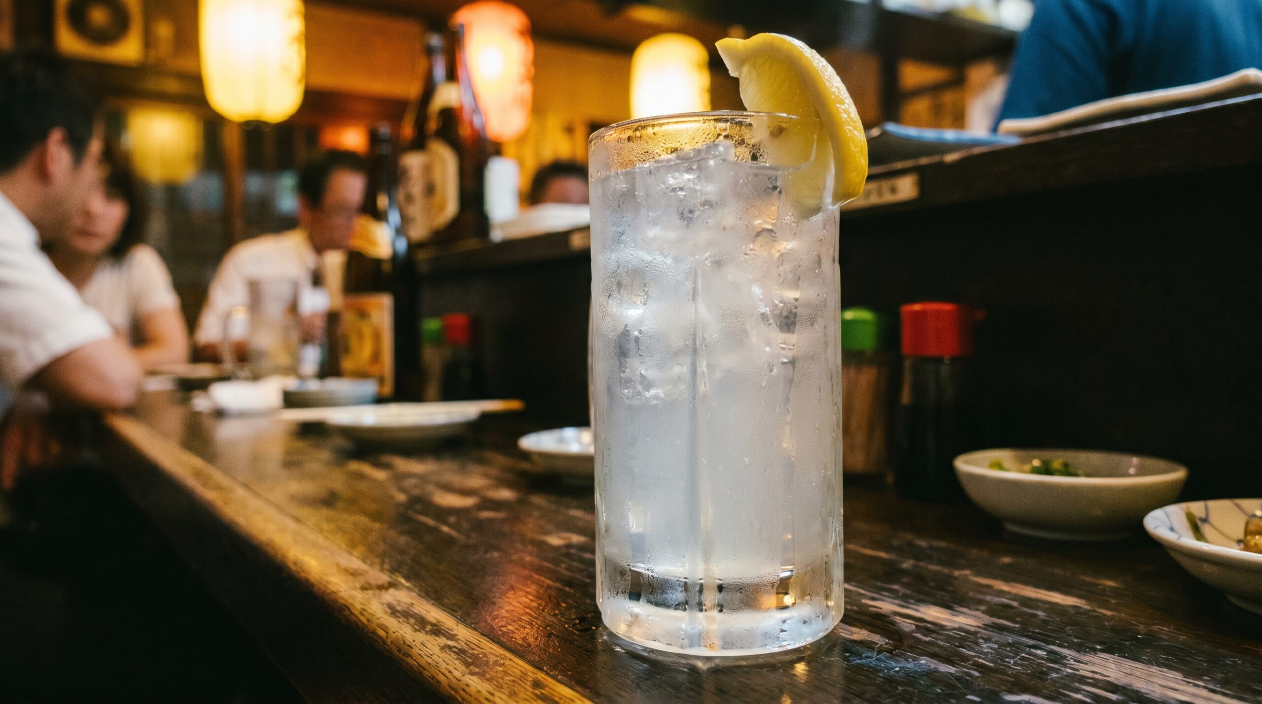 Lemon Sour: Japan's Default Drink, and What That Means 1 A tall glass of lemon sour on a dark izakaya counter — condensation on the glass, a wedge of real lemon on the rim, ice visible inside. The drink is pale gold. The light is warm.