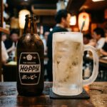 Hoppy: The Drink That Tests Whether a Place Knows What It's Doing A frosty Hoppy bottle beside a frozen mug of shochu on an izakaya counter. The mug is ice-cold, frosted white. The Hoppy bottle is classic design — unchanged for decades. Dark counter, warm ambient light.